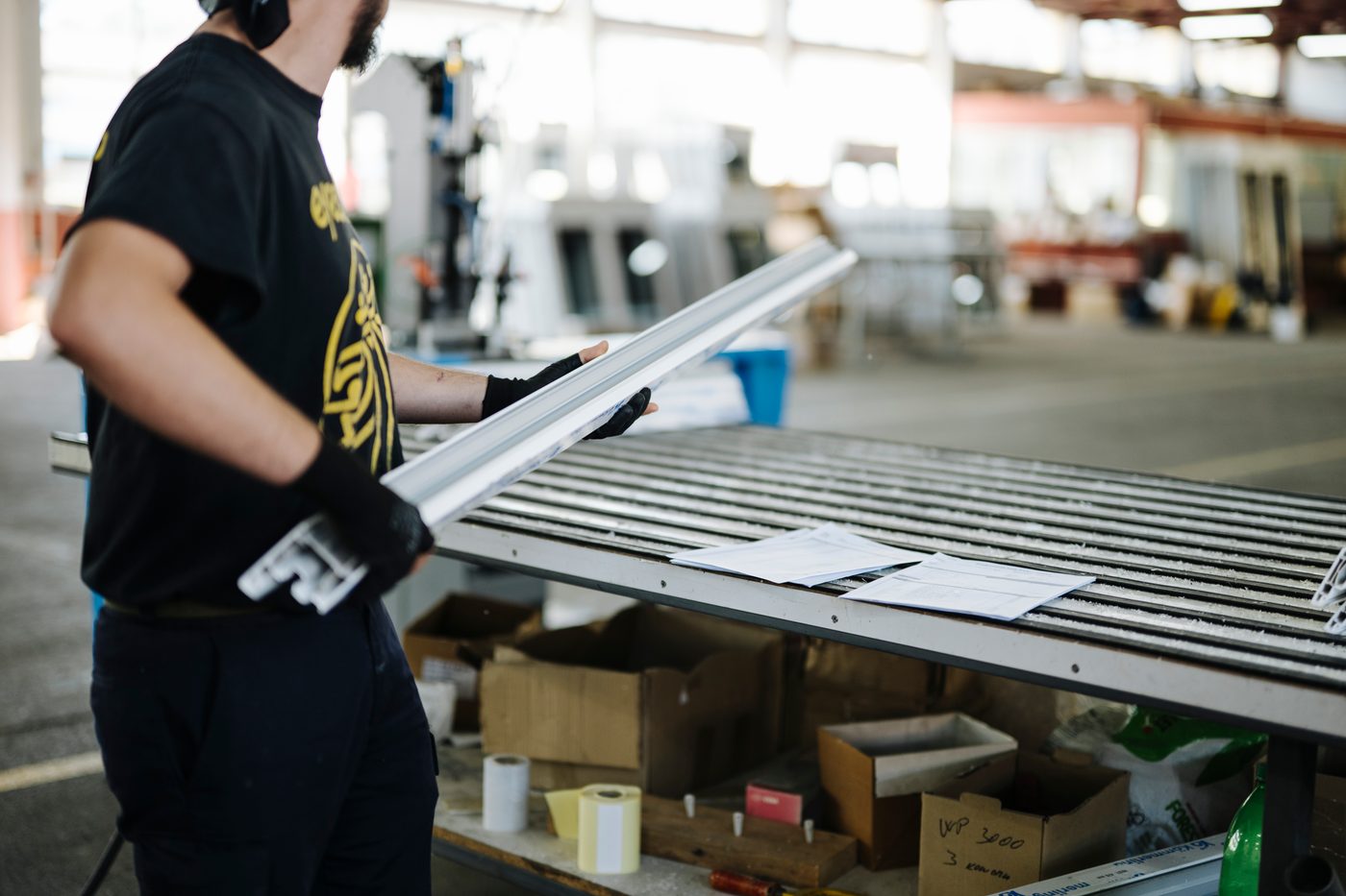 A worker in gloves handling a component at a staging table, parts boxed in bins with build sheets laid out below.