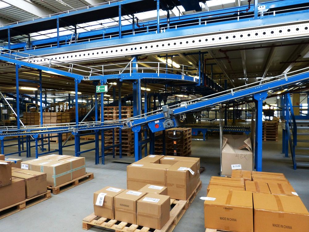 Conveyor lines running through a distribution facility past palletised and boxed stock.